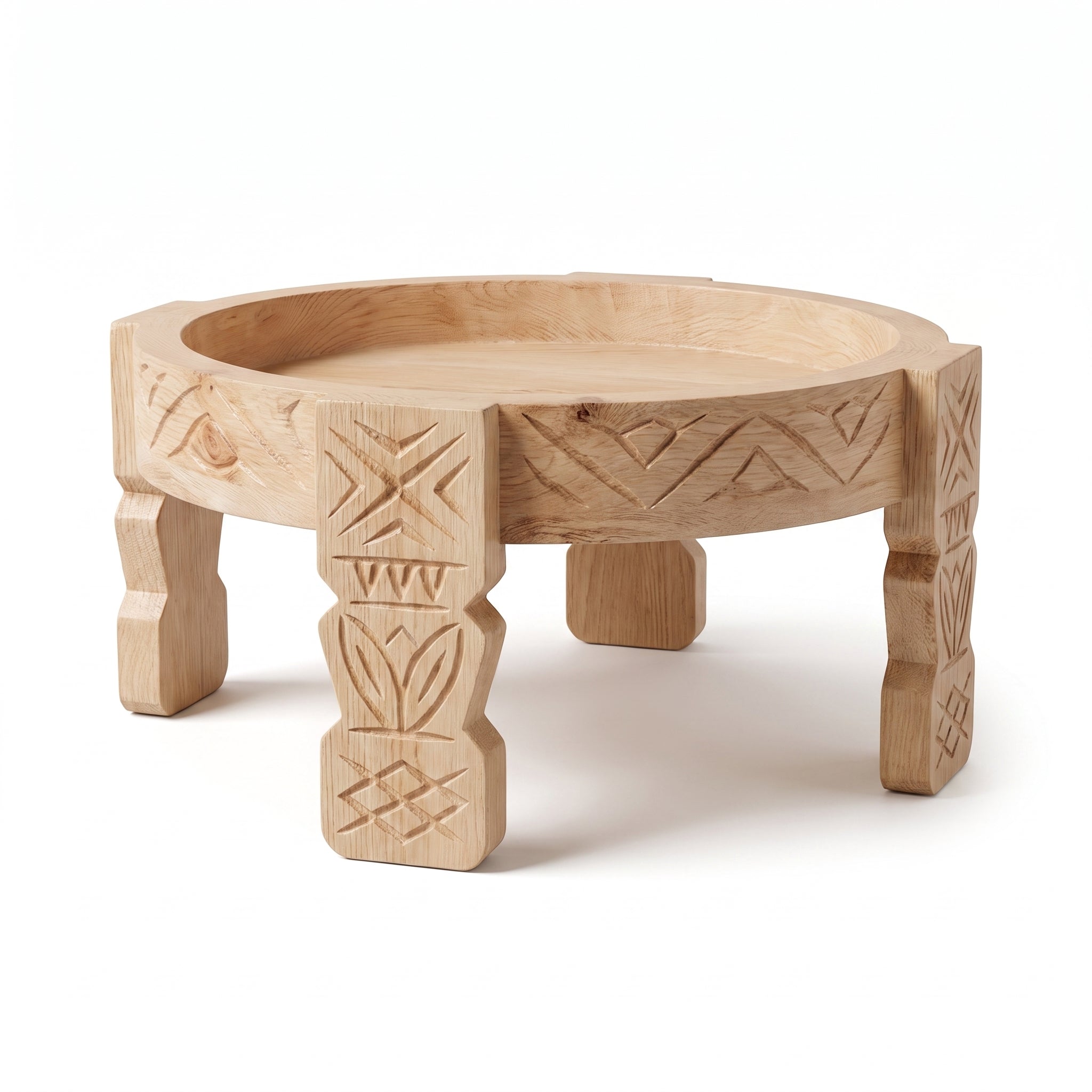 A round, low wooden stand or tray table with carved geometric and tribal-style patterns on its legs and rim, shown on a clean white background.