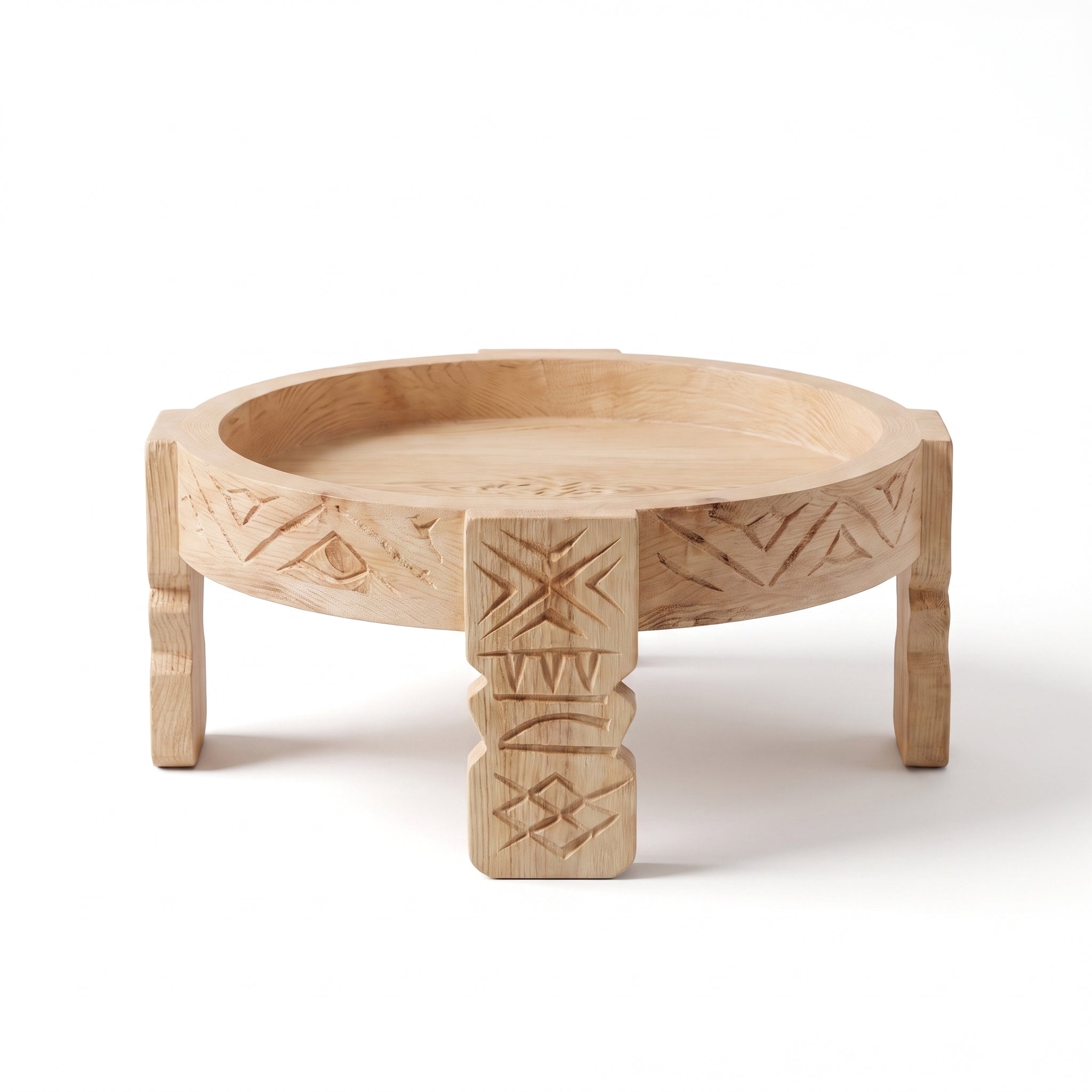 A light natural wood serving tray table with carved geometric patterns on the rim and pedestal legs, shown on a clean white background.