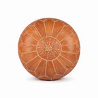 Top view of a caramel tan leather pouf with white stitching and a central embroidered medallion