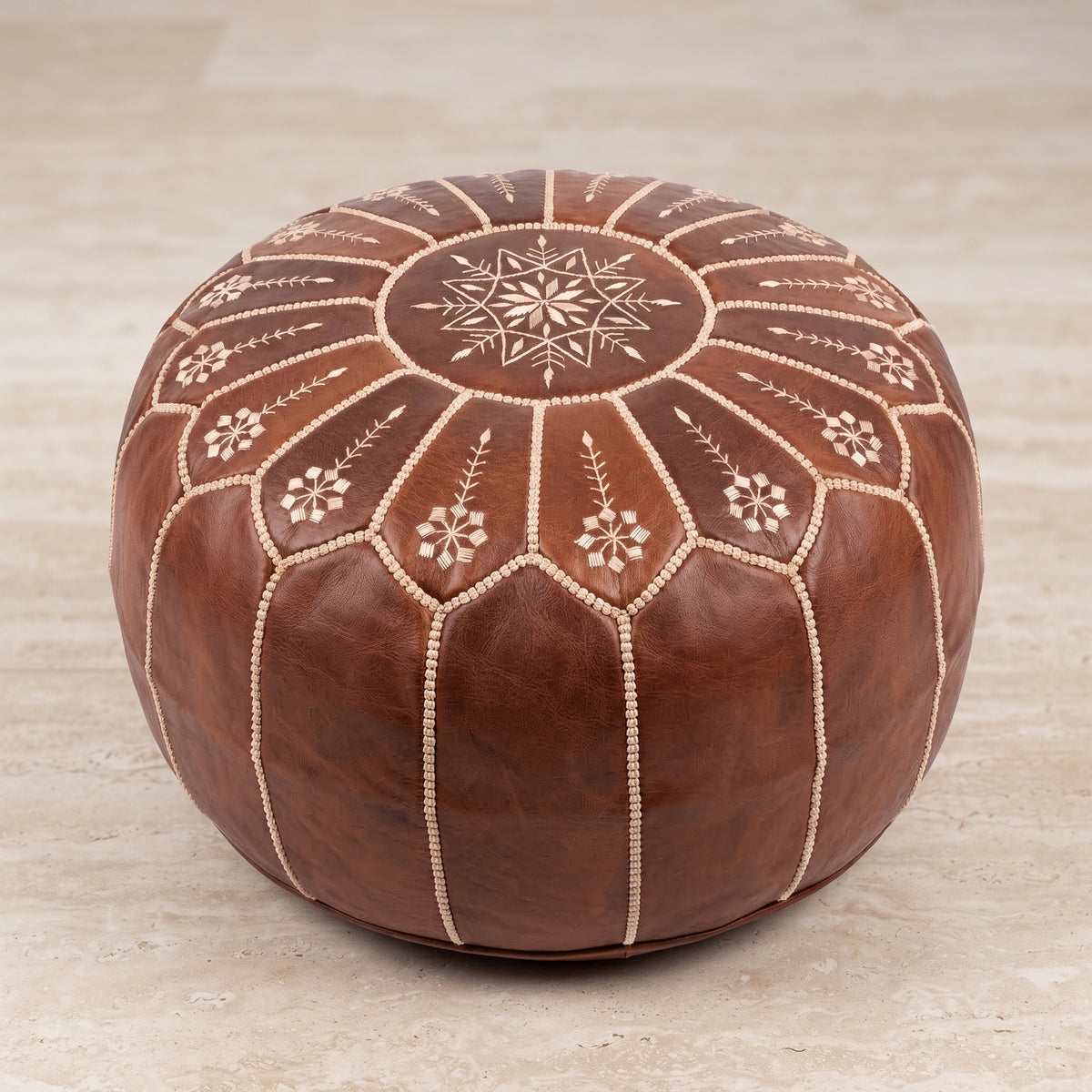 Brown leather pouf with white floral stitching on a light stone floor
