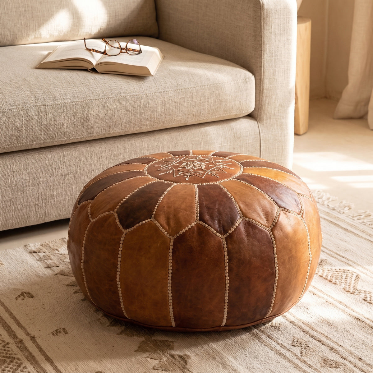 Two-tone brown Moroccan leather pouf with star embroidery beside a sofa on a woven rug