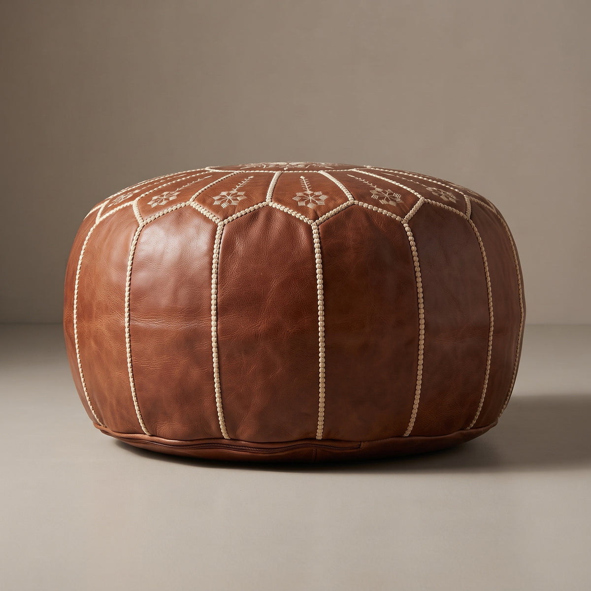 Side view of a brown leather pouf with white seams against a dark neutral background
