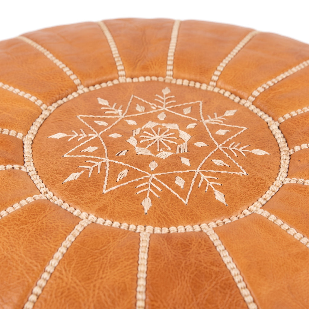 Close-up of white star embroidery and seams on a caramel tan leather pouf