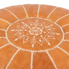 Close-up of white star embroidery and seams on a caramel tan leather pouf