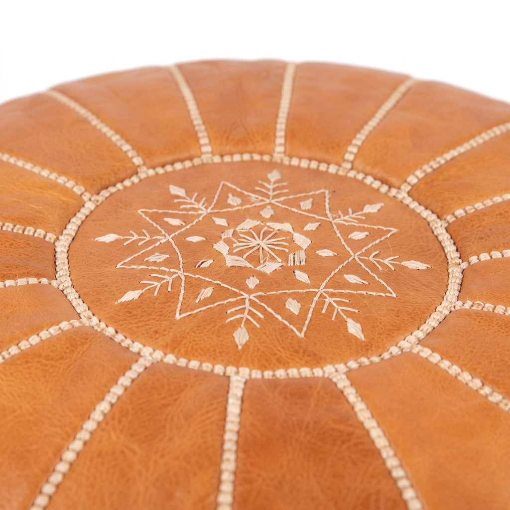 Detail of white star embroidery on the top of a caramel tan leather pouf