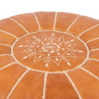 Detail of white star embroidery on the top of a caramel tan leather pouf