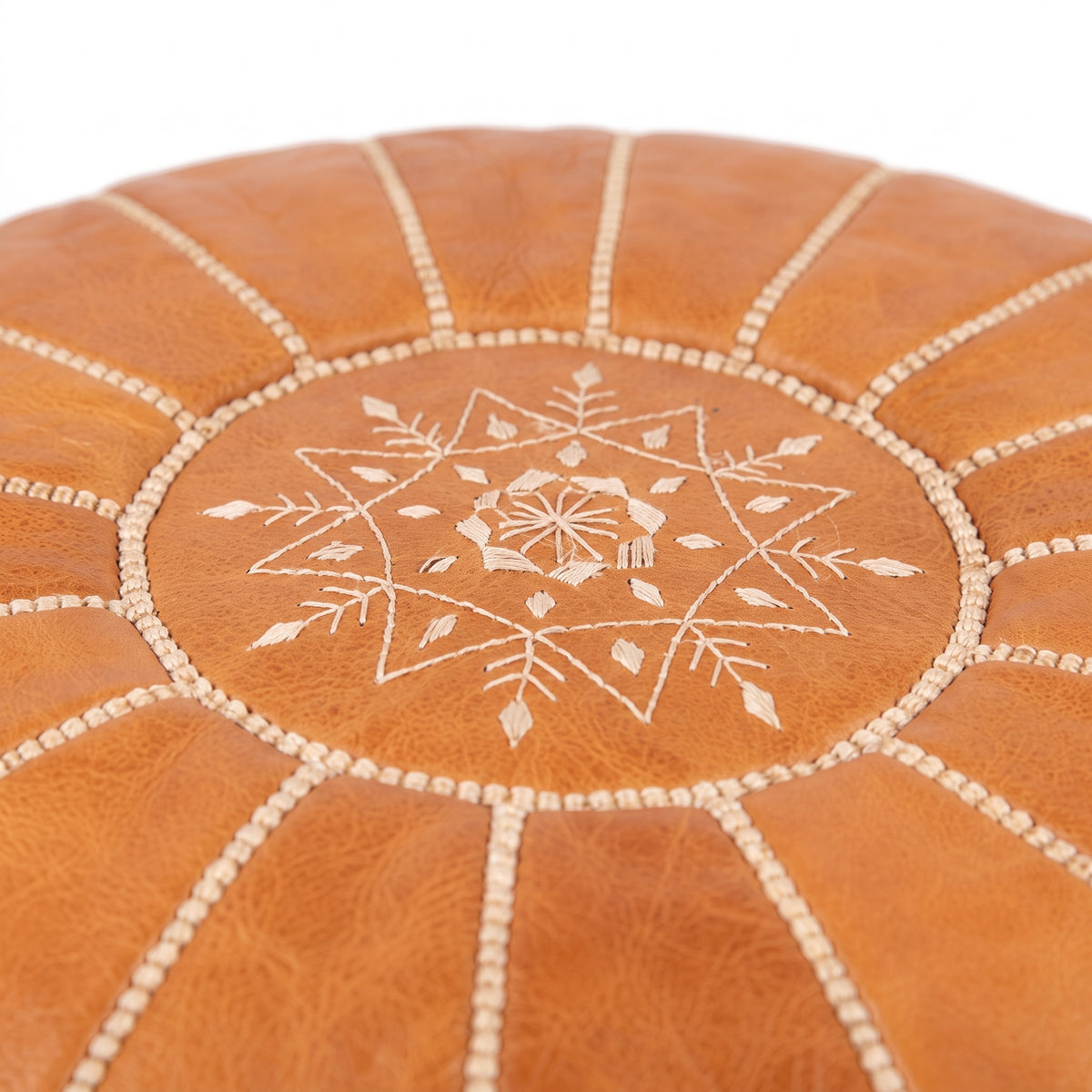 Detail of white star embroidery on the top of a caramel tan leather pouf
