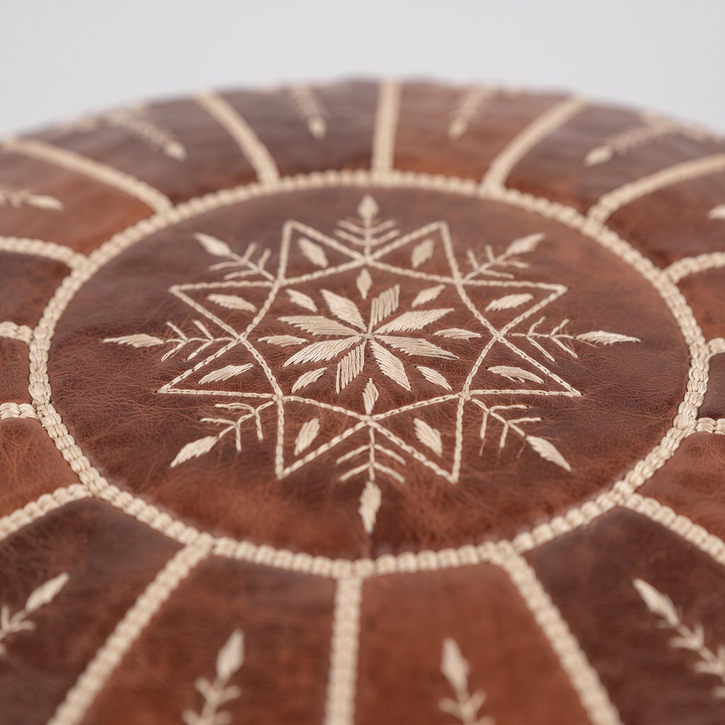 Close-up of a white embroidered star medallion on a brown leather pouf