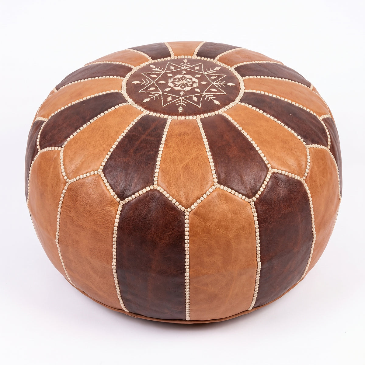 Angled view of a two-tone brown leather pouf with white seams and embroidered top