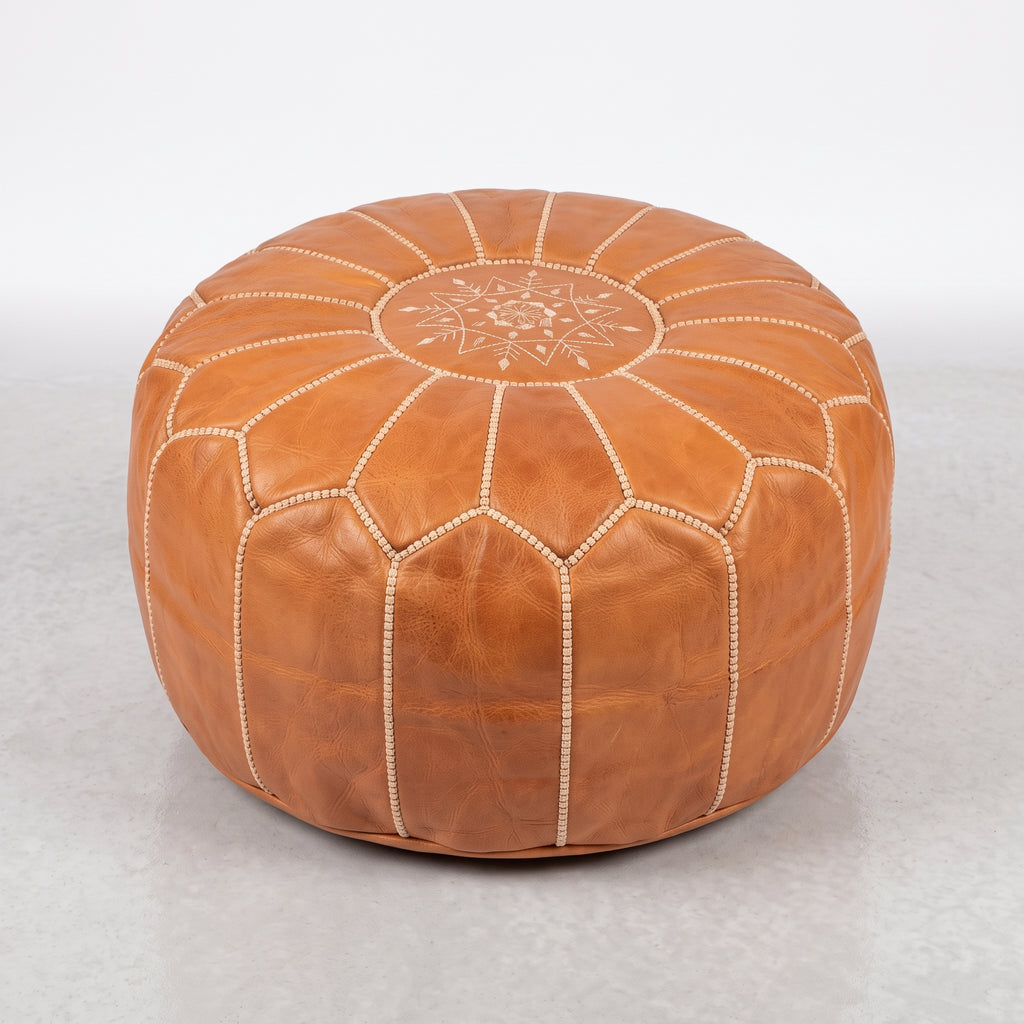 Angled view of a caramel tan leather pouf with white panel stitching