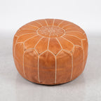 Angled view of a caramel tan leather pouf with white panel stitching