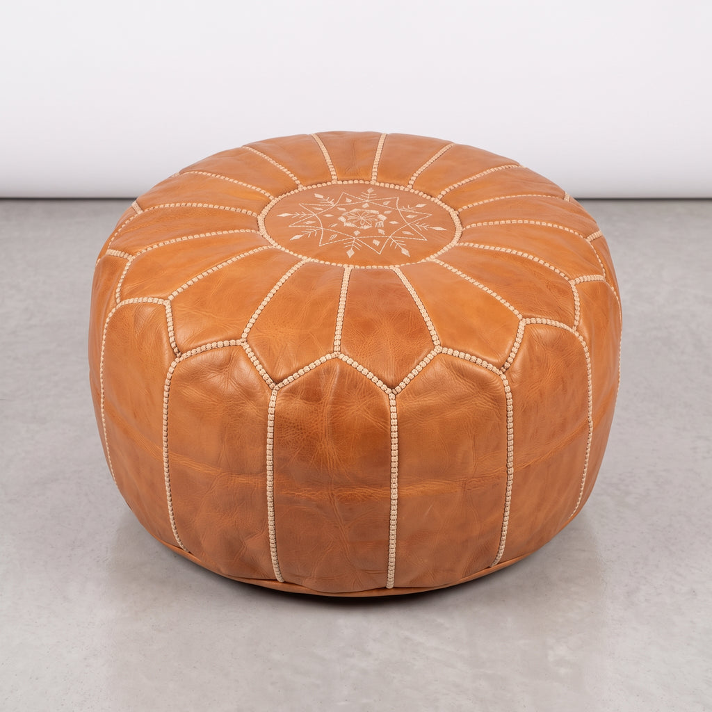 Caramel tan Moroccan leather pouf with white stitching on a light floor
