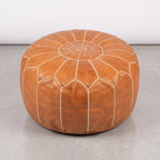 Caramel tan Moroccan leather pouf with white stitching on a light floor