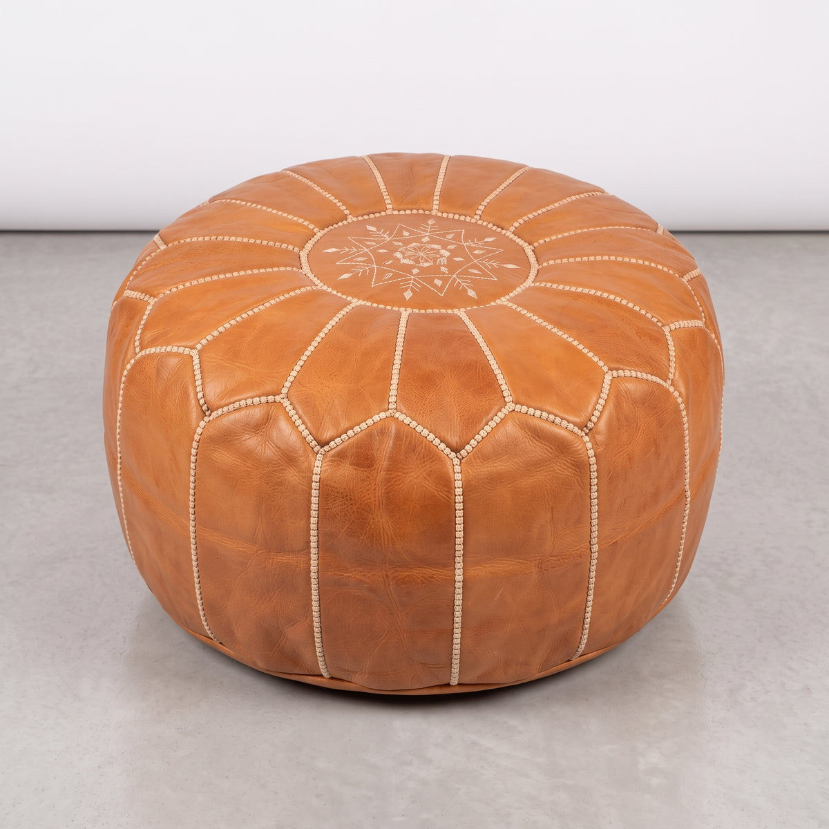 Caramel tan Moroccan leather pouf with white stitching on a light floor