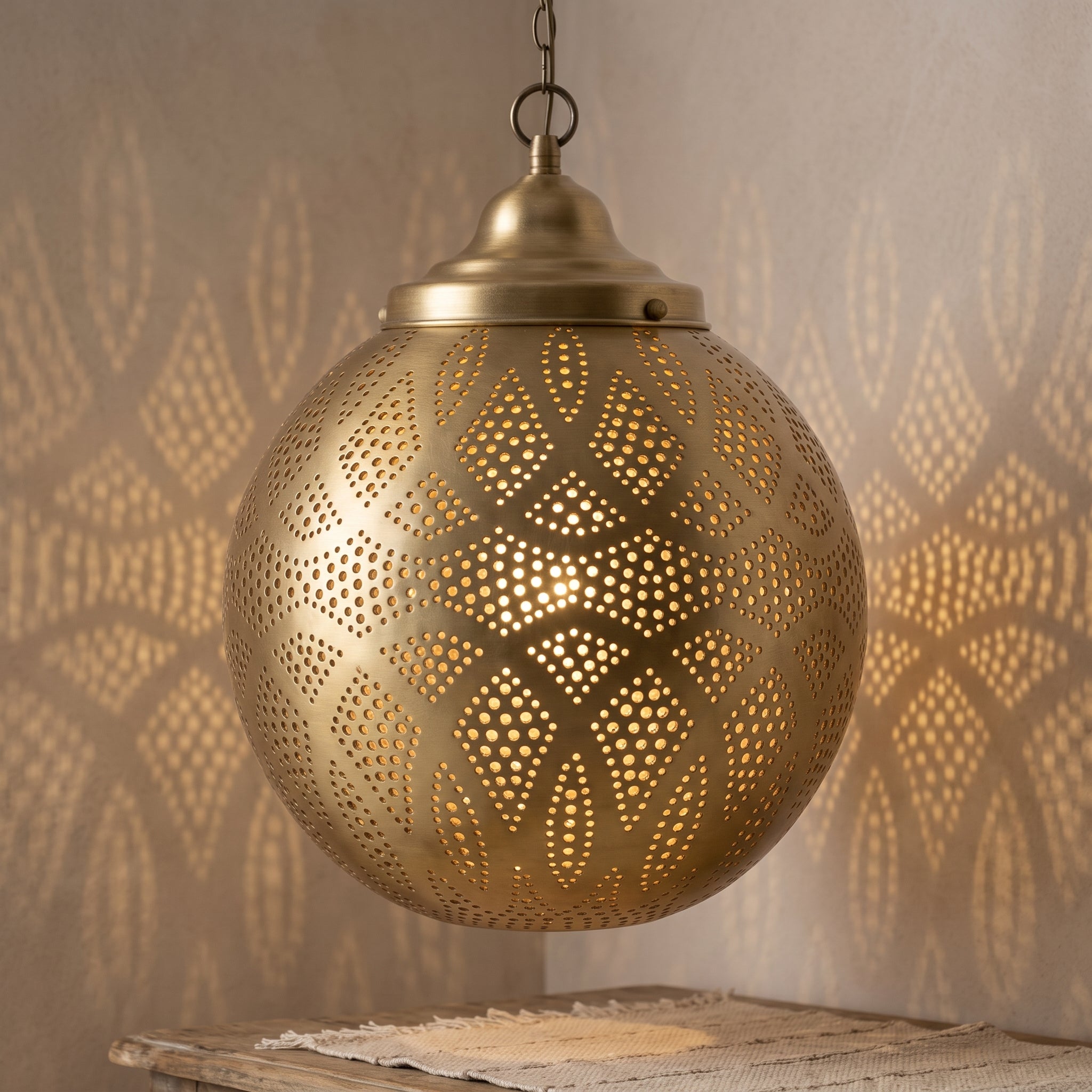 Lit brass filigree pendant casting patterned light on a neutral wall