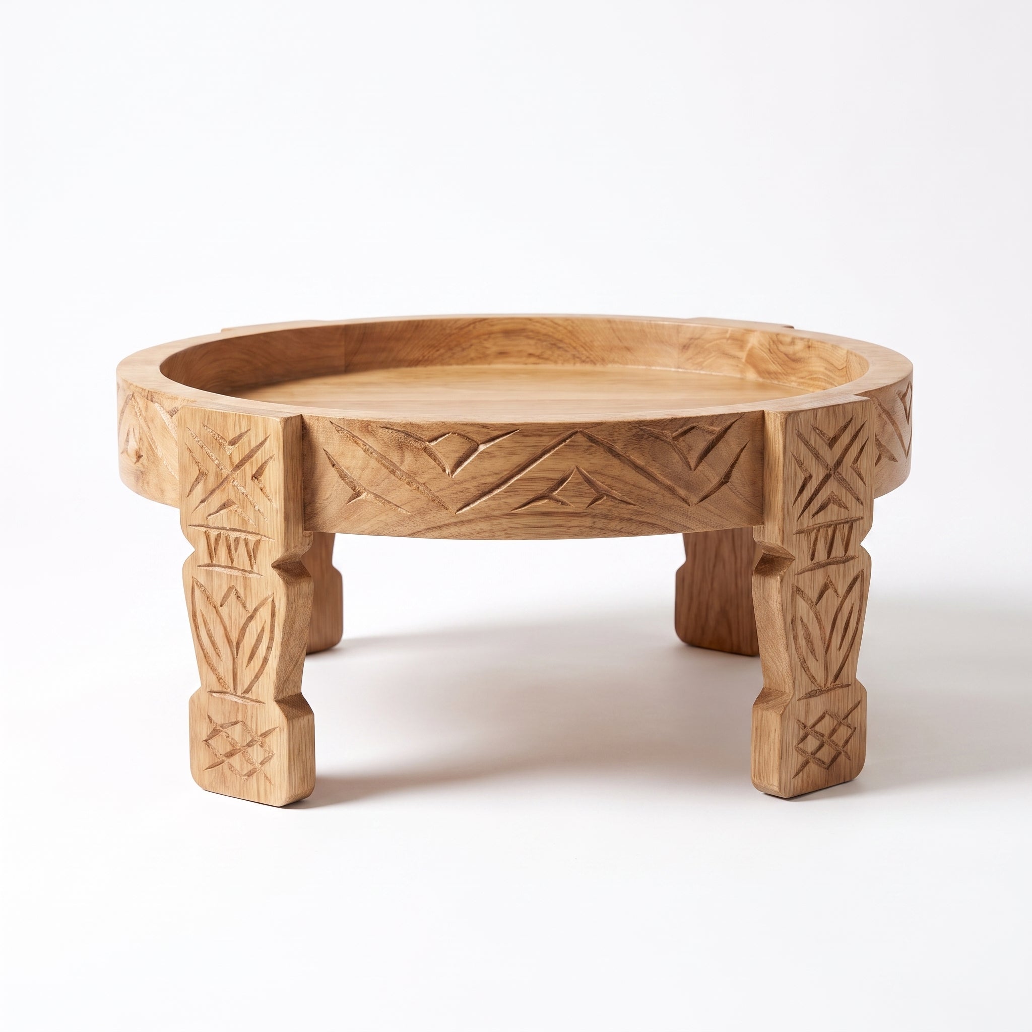 A round, low wooden serving tray with carved geometric patterns on the rim and four carved legs, shown on a clean white background.