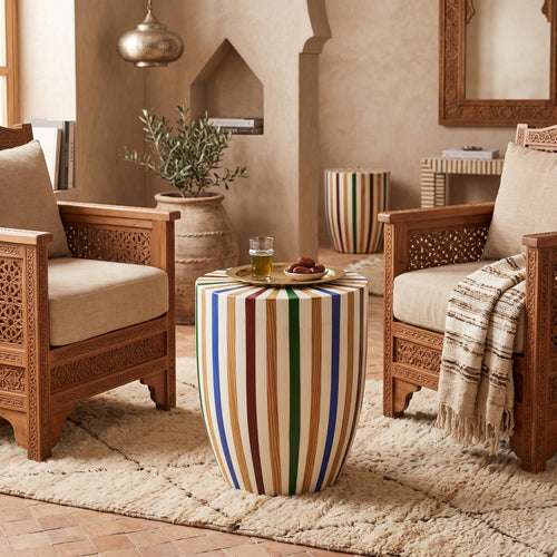 Multicolored striped wooden drum stool with a vase between cushioned wooden armchairs