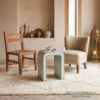 Turquoise striped arch side table with a tea set between wooden and cream lounge chairs