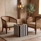 Black and white striped cube side table with a tea tray between two cane armchairs