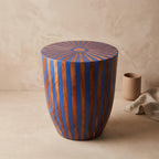 Angled view of a blue and orange striped wooden drum table against a beige wall