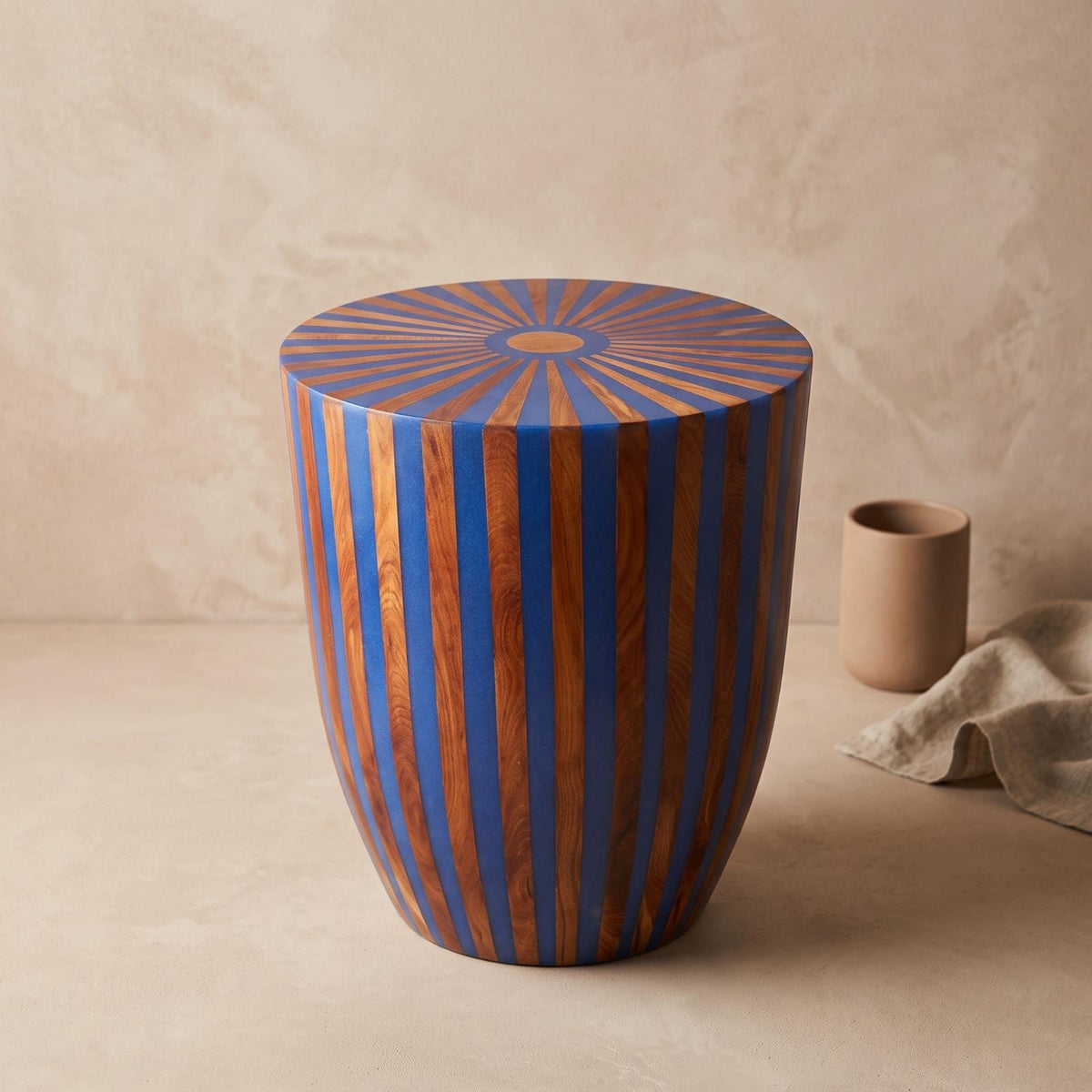 Angled view of a blue and orange striped wooden drum table against a beige wall