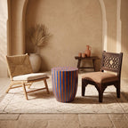 Blue and orange striped drum table between wooden chairs in a warm beige interior