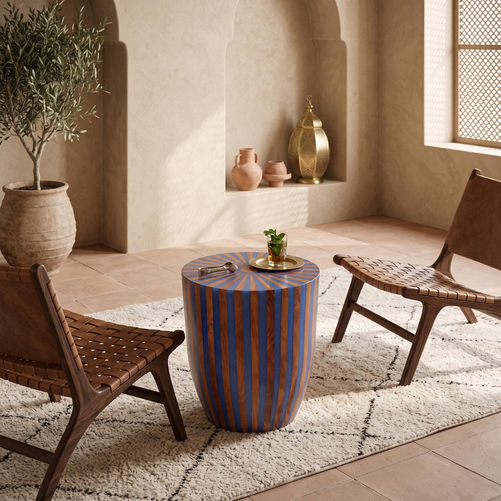 Blue and orange wood-inlay drum table between cushioned chairs near a bright window