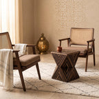 Chevron-inlaid dark wooden hourglass table with a small cup between two armchairs