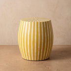 Yellow striped wooden drum side table with a radial sunburst top against a beige wall