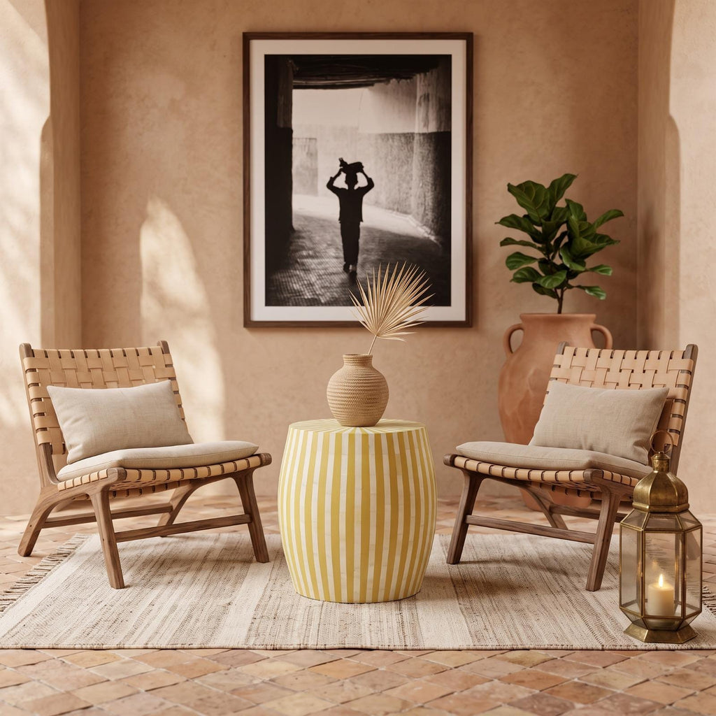 Yellow striped drum table with a vase between woven chairs beneath a framed photograph