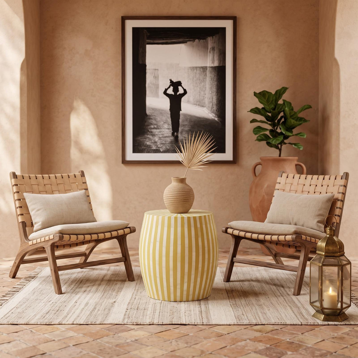 Yellow striped drum table with a vase between woven chairs beneath a framed photograph
