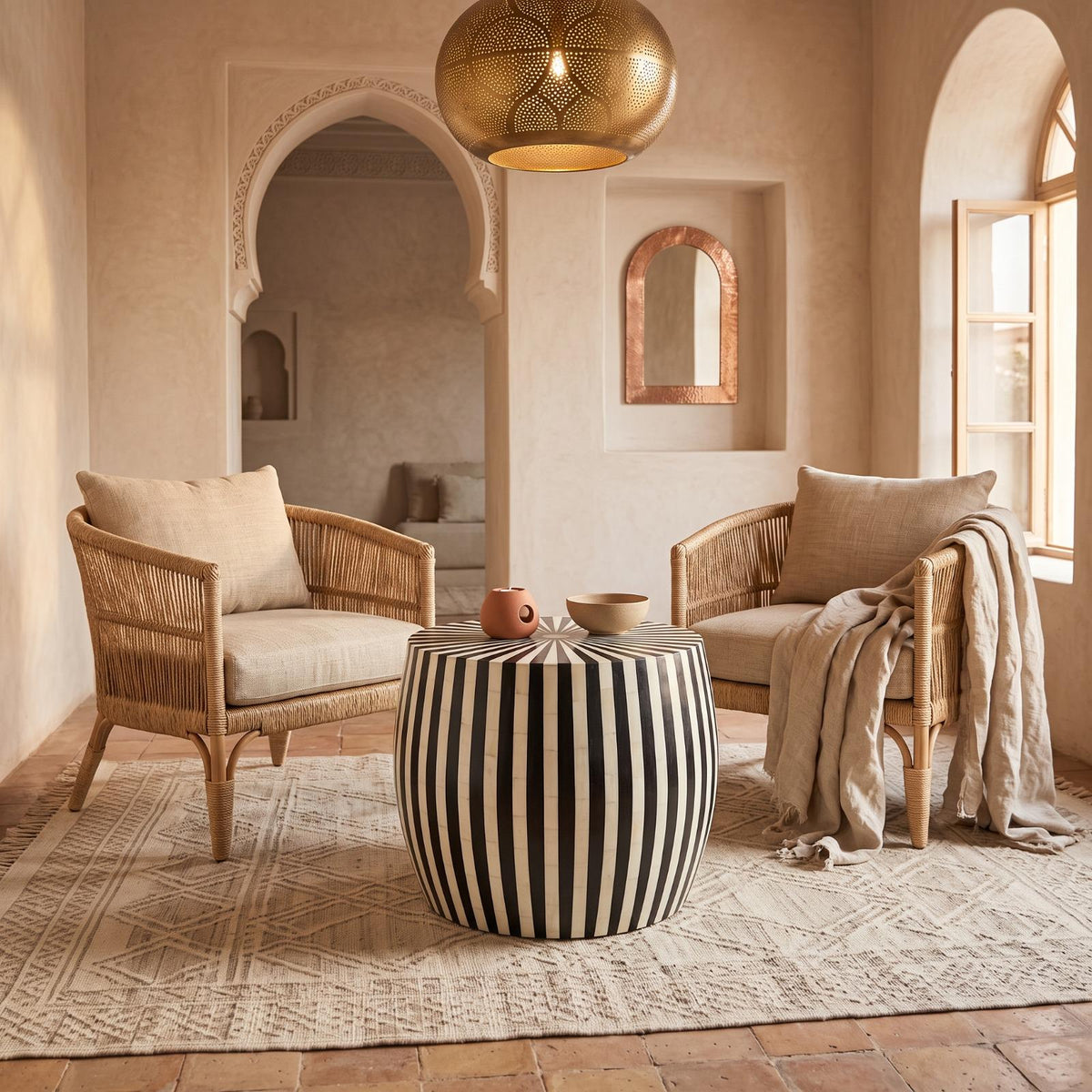 Black and cream striped drum side table between cushioned armchairs beneath a brass pendant