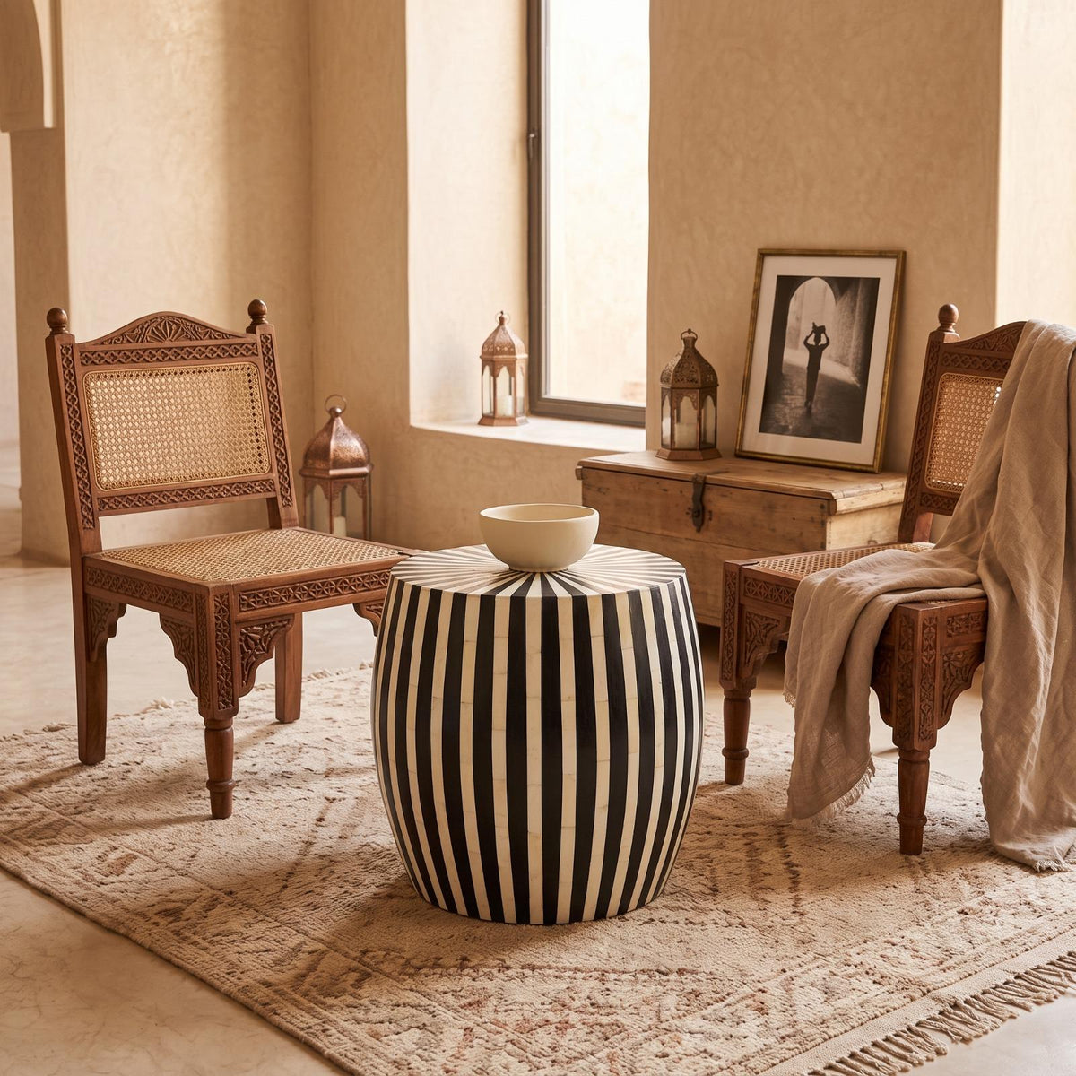 Black and cream striped drum side table topped with a white bowl between wooden chairs