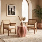 Red and cream striped drum side table between cushioned chairs beside an arched window