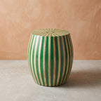 Green striped wooden drum side table with a radial sunburst top against a beige wall