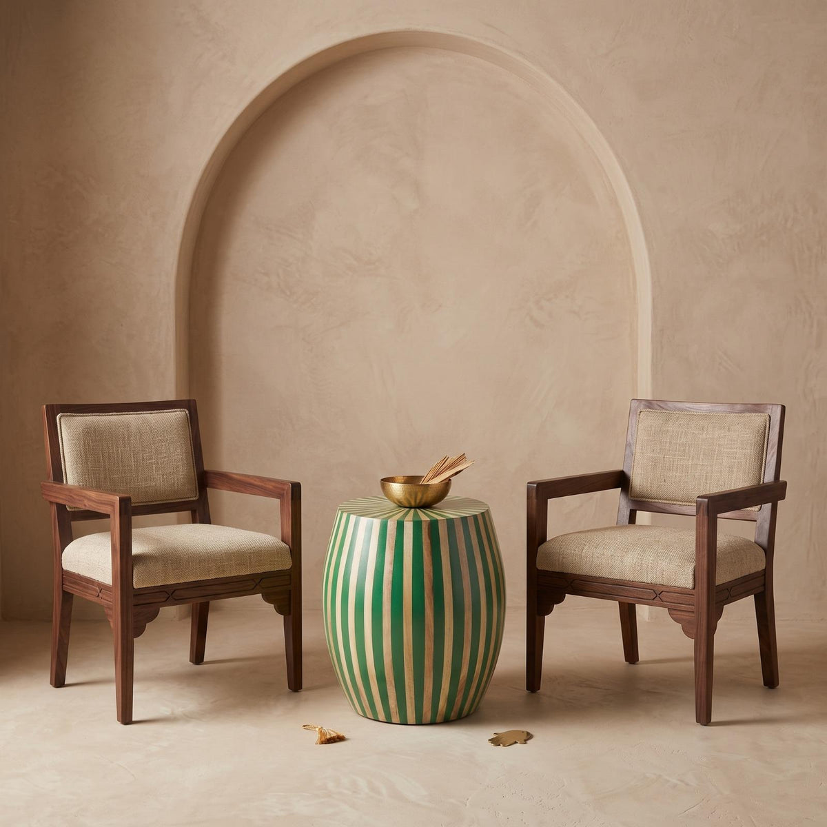 Green striped drum table topped with a brass ornament between wooden chairs beneath an arched niche