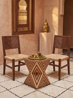 Geometric wooden hourglass table with light and dark stripes between two woven-seat chairs