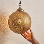 Hand held beneath a brass globe pendant with floral medallion perforations