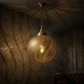 Spiral Bands brass pendant casting curved patterns in a dark living room