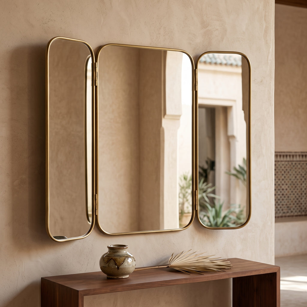 Moroccan brass triptych wall mirror above a wooden console with a ceramic vase against a textured beige wall