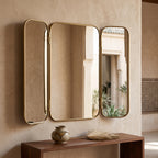 Moroccan brass triptych wall mirror above a wooden console with a ceramic vase against a textured beige wall