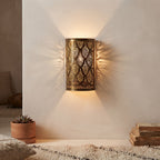 Brass wall sconce with teardrop motifs casting warm patterned light onto a beige wall