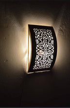 Illuminated curved floral brass wall sconce casting light onto a dark wall