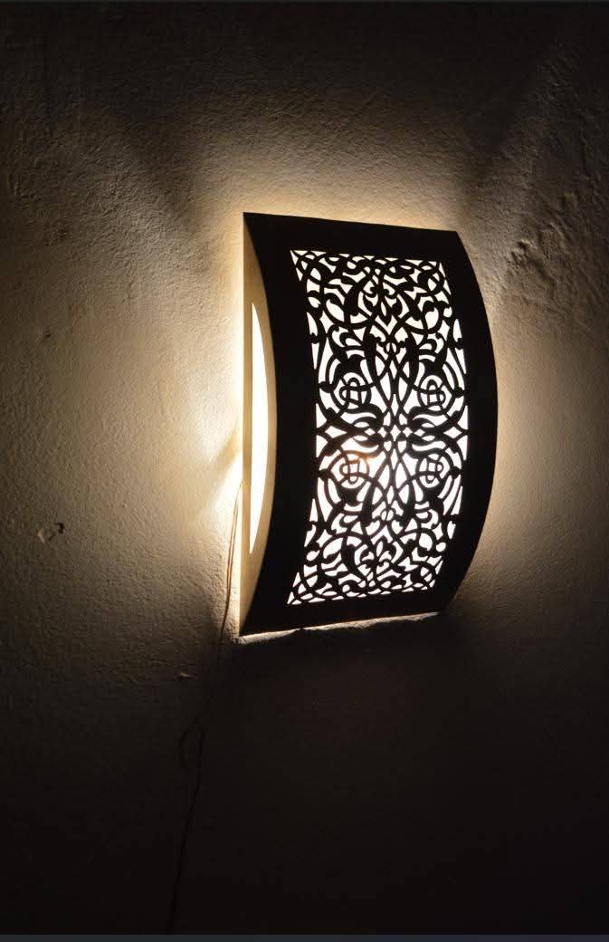 Illuminated curved floral brass wall sconce casting light onto a dark wall