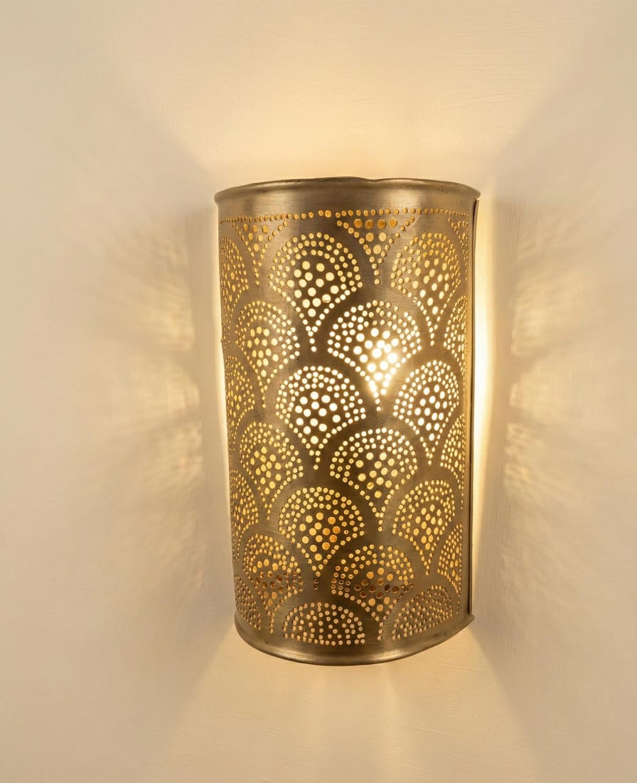 Illuminated brass wall sconce with overlapping teardrop motifs on a beige wall