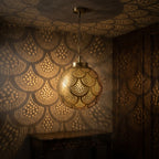 Illuminated brass globe pendant projecting scalloped light patterns in a dark room
