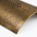 Close-up of the curved brass surface and tiny perforations of an arabesque wall sconce